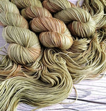 hand dyed muted greens and browns in 3 twisted skeins, laying on one open skein.  One a wood effect background.